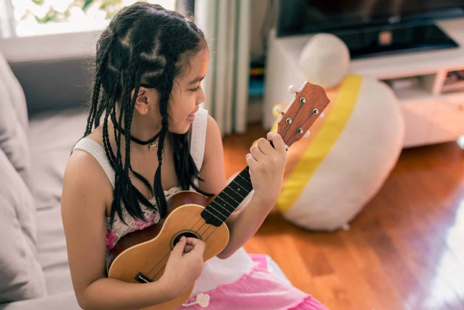 A young student holding a ukulele at home